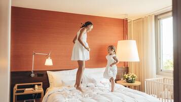Habitación de hotel con cama, mesita de noche con lámpara, una pequeña mesa con un florero y una ventana con cortinas.