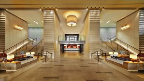 A spacious lobby with a central reception desk, two symmetrical staircases, and a modern ceiling design.