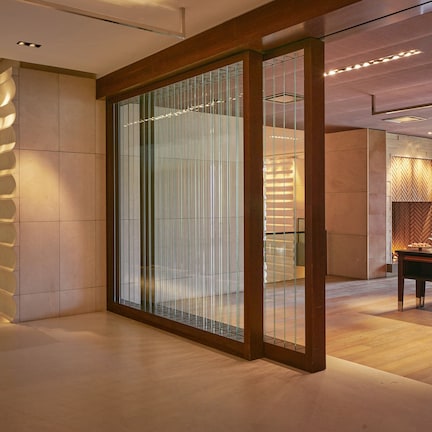 A modern interior with a glass partition, wooden flooring, and a dining area with a herringbone-patterned wall.
