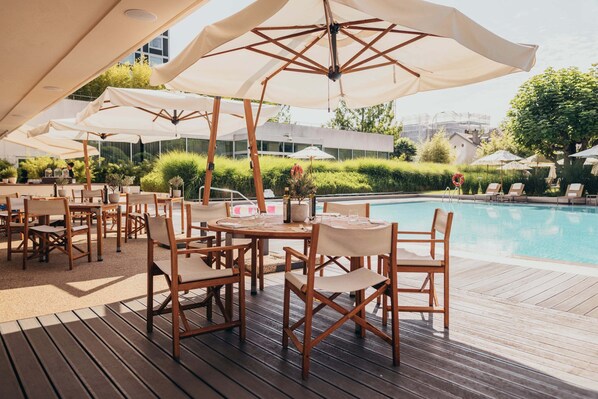 An outdoor pool area with wooden deck, lounge chairs, and umbrellas.