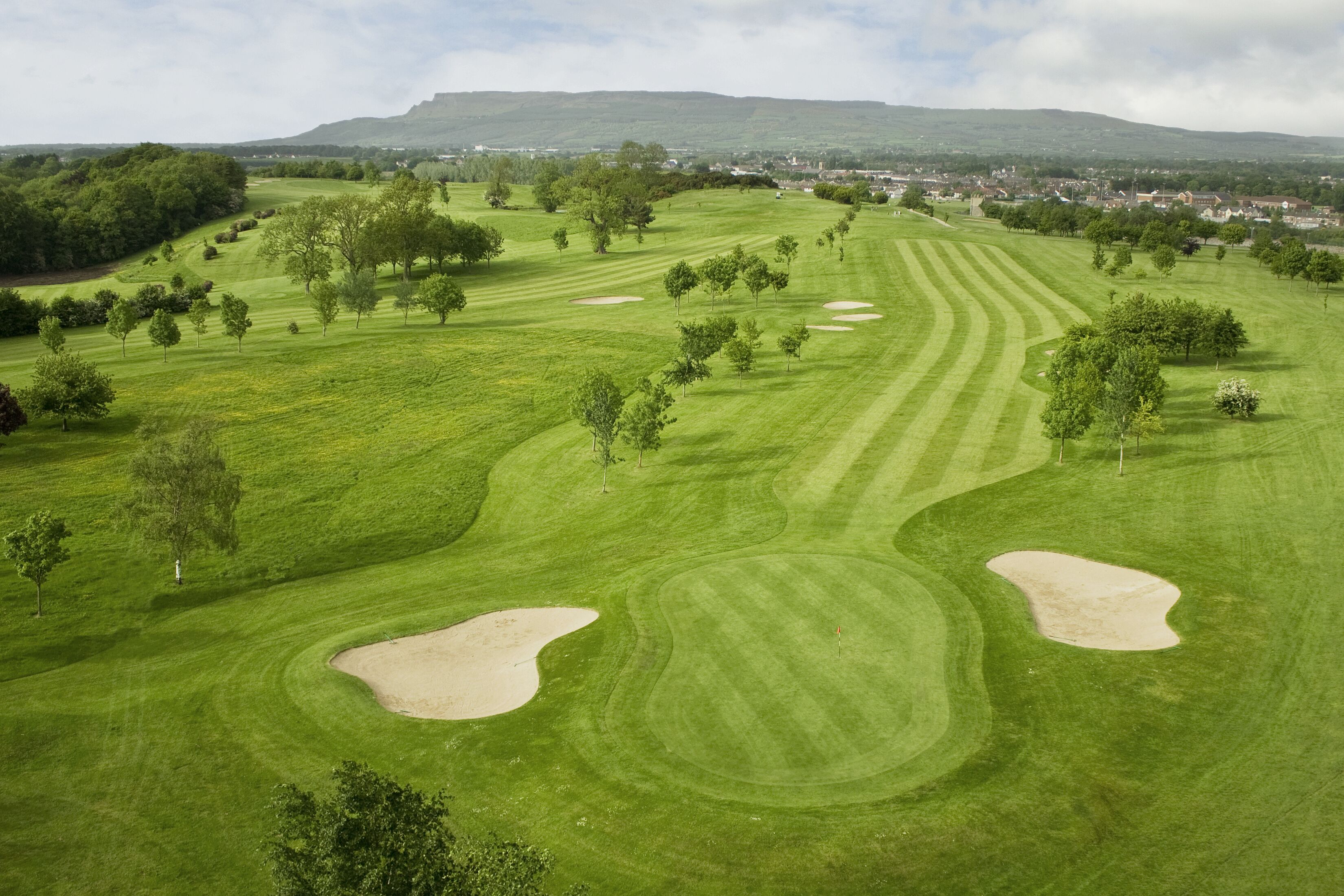 A golf course with sand bunkers, trees, and a distant town.