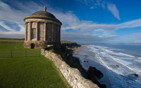 A historic stone building with a dome, located by a coastal cliff overlooking the ocean.