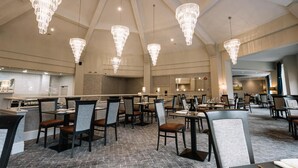 A spacious dining area with multiple tables and chairs, large chandeliers, and a modern kitchen in the background. - Roe Valley Resort (Limavady)