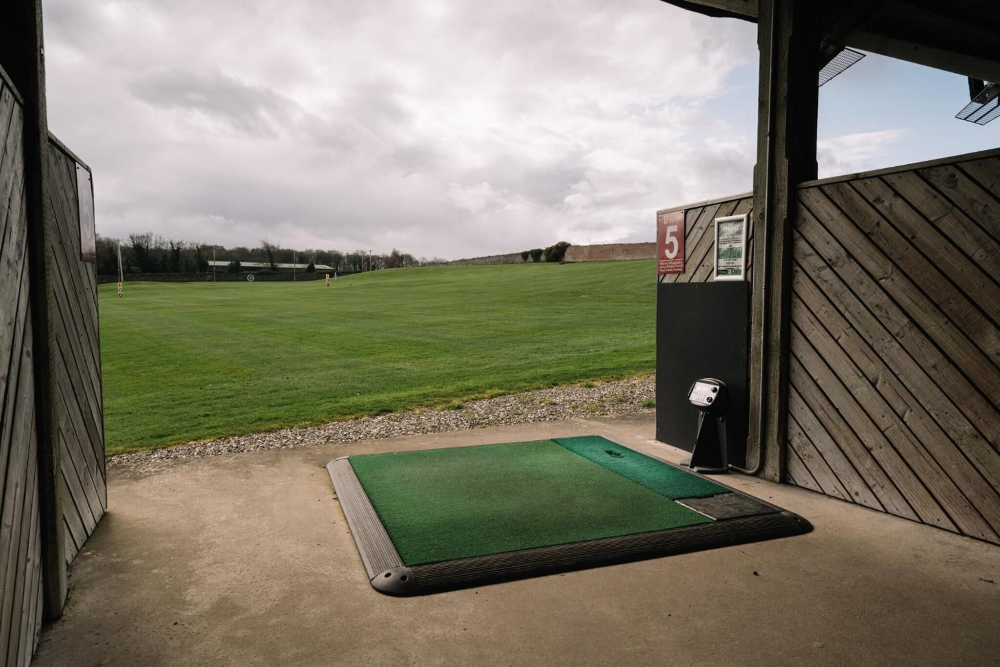 A golf driving range with a green mat at the entrance, a scorecard, and a wooden building structure.