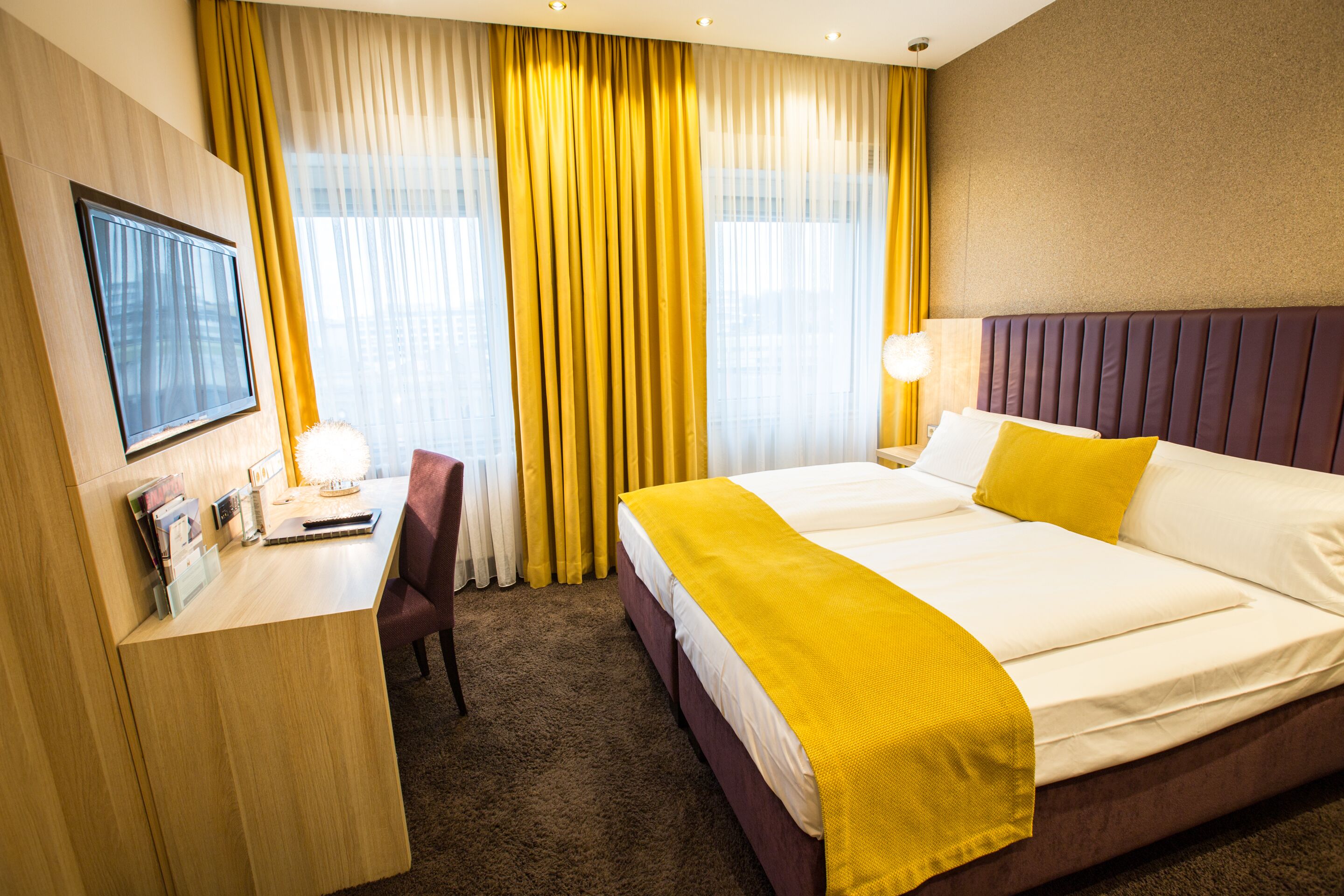 Ein Hotelzimmer mit Bett, Schreibtisch, Sessel, Fernseher und Vorhängen.