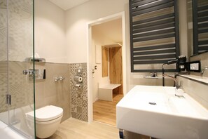 Features a sleek sink, glass-enclosed shower, and minimalist toilet in a calm, inviting space.