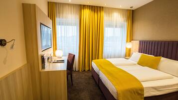 A hotel room with a bed, a desk, a chair, and a television.