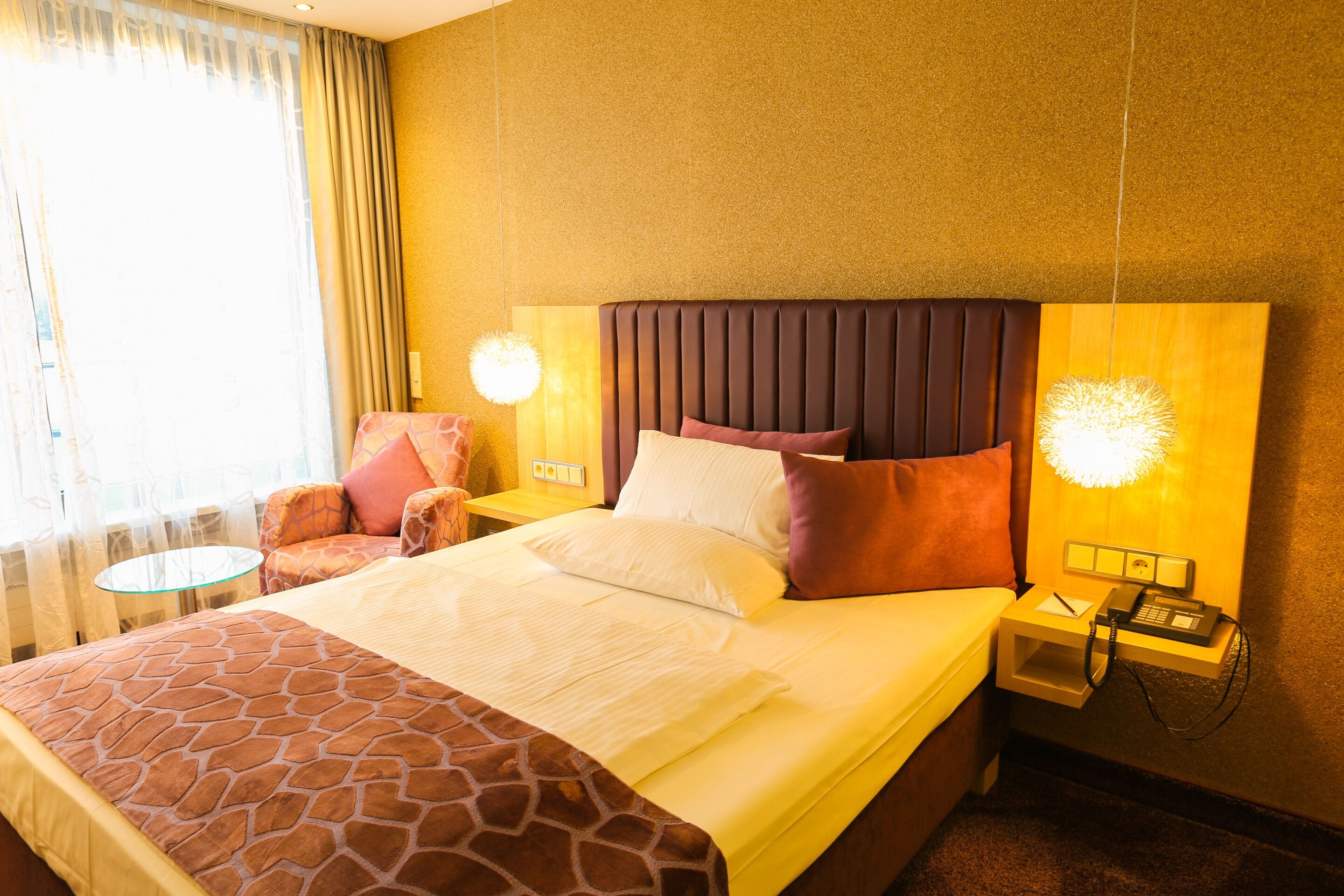 A hotel room with a large bed, a bedside table with a lamp, a chair, and a small table.