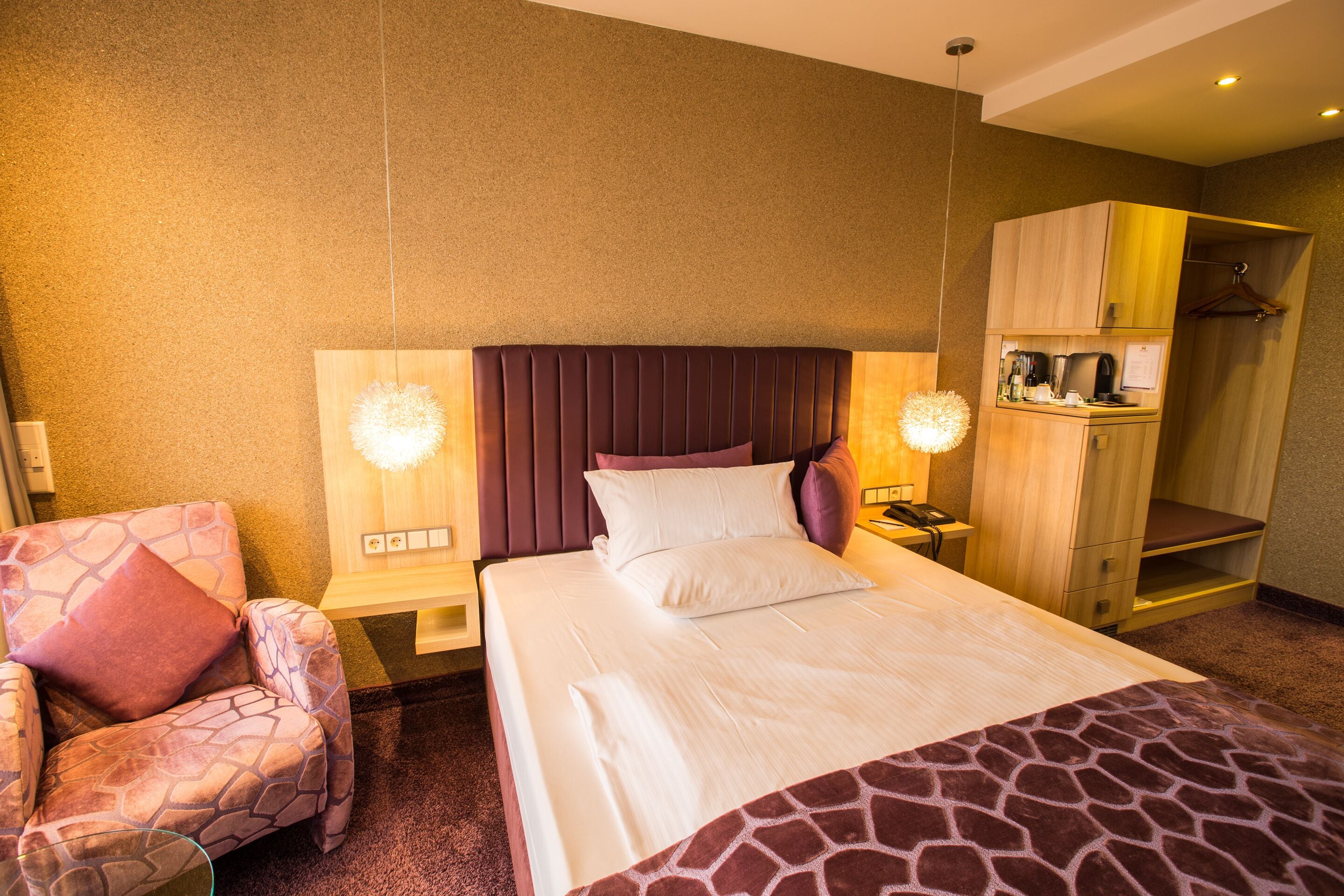 Ein Hotelzimmer mit einem großen Bett, einem Sessel, einem Kleiderschrank und einem Schreibtisch mit einer Lampe.