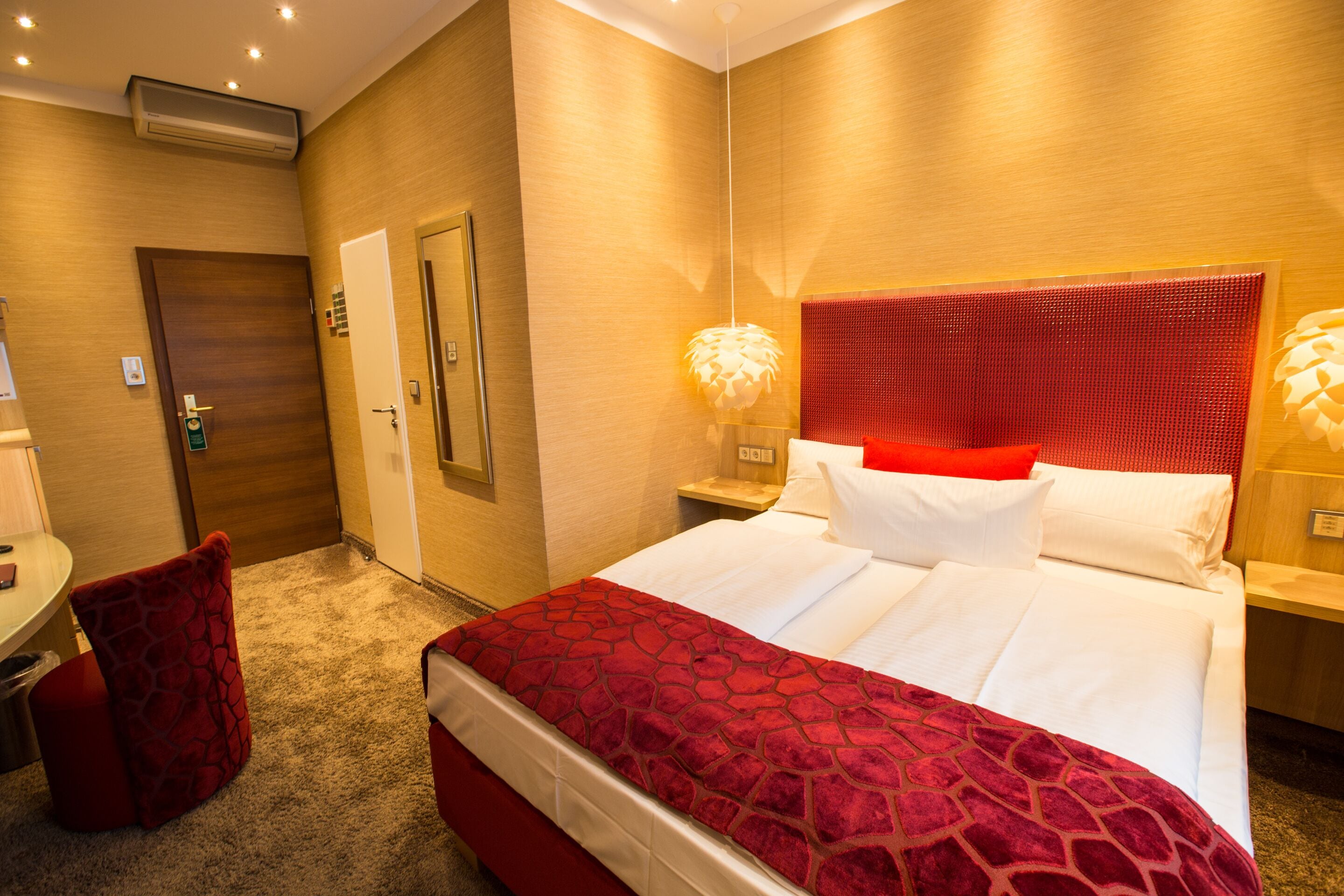Habitación de hotel con una cama grande, una pared de acento roja, un escritorio con una silla y un cojín rojo.