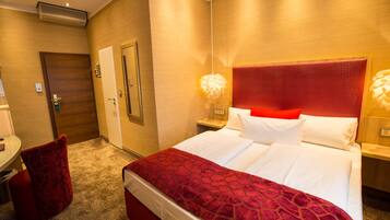 Habitación de hotel con una cama grande, una pared de acento roja, un escritorio con una silla y un cojín rojo.