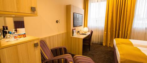 A hotel room with a bed, a desk with a chair, a television, and a minibar.