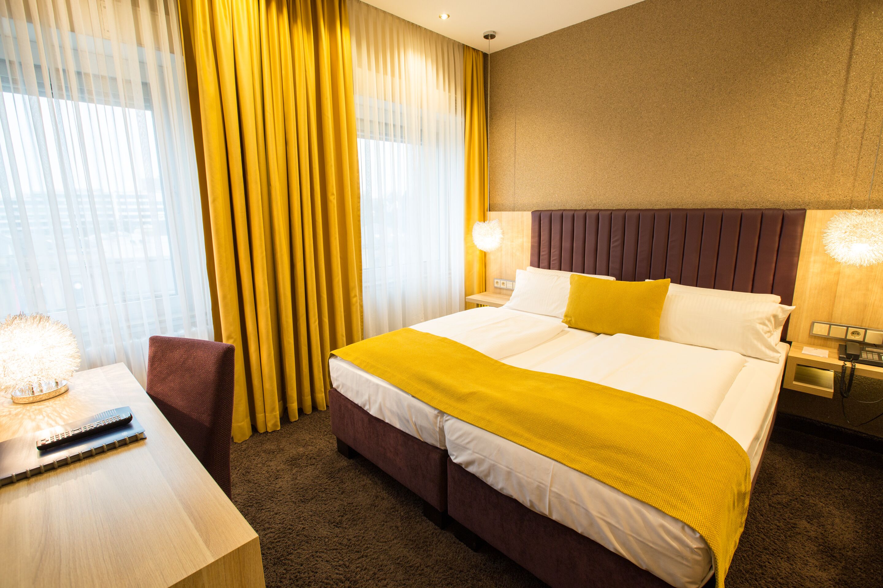 A hotel room with a large bed, a desk, a chair, and a nightstand with a lamp.