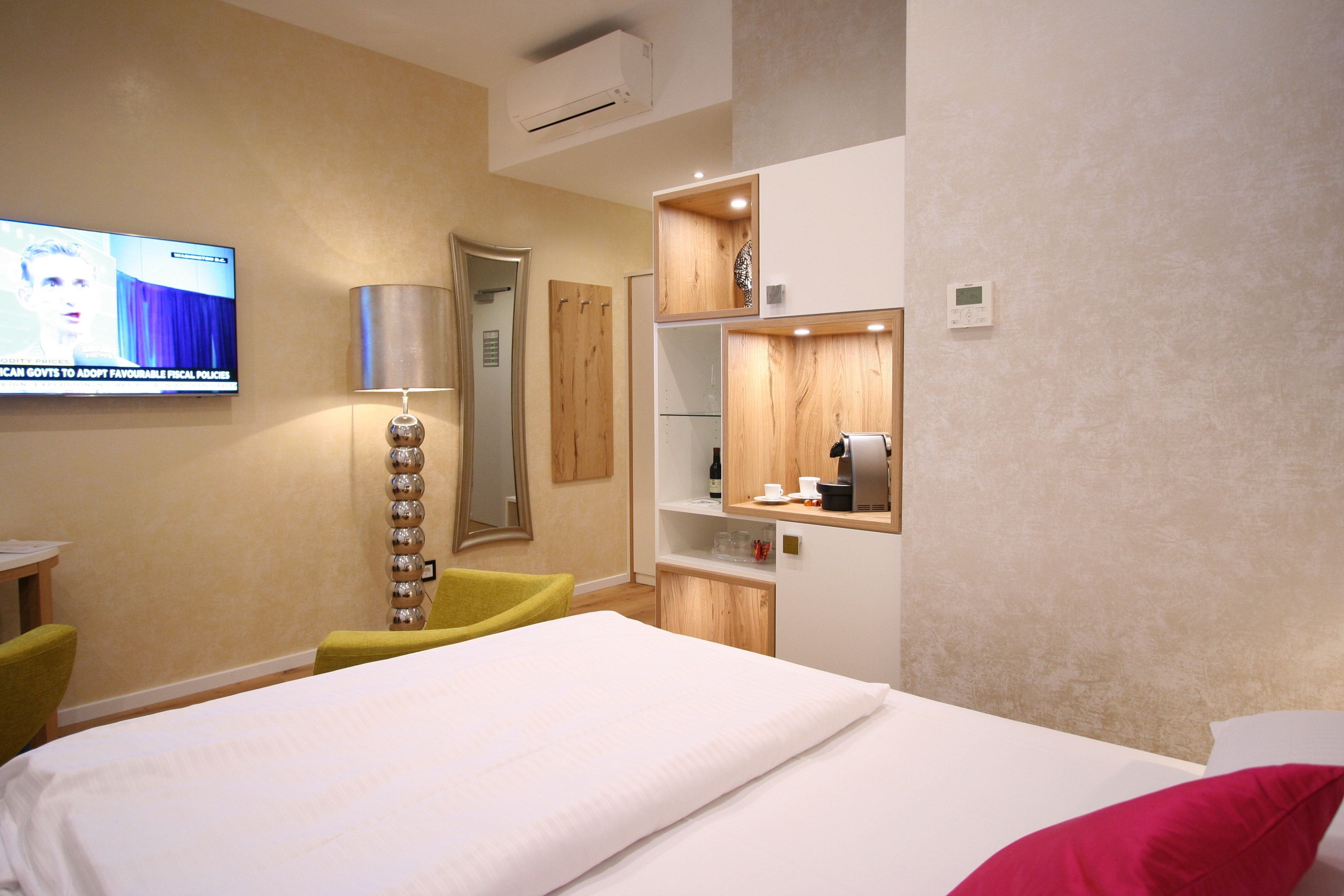 Habitación de hotel con una cama, un televisor en la pared, un escritorio con silla y un espejo.
