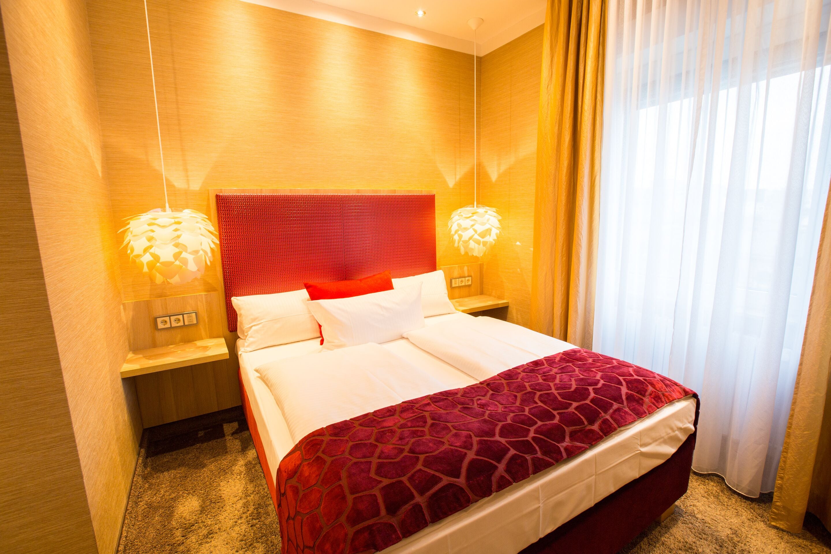 Quarto de hotel com uma cama grande, cabeceira vermelha e duas luminárias laterais.