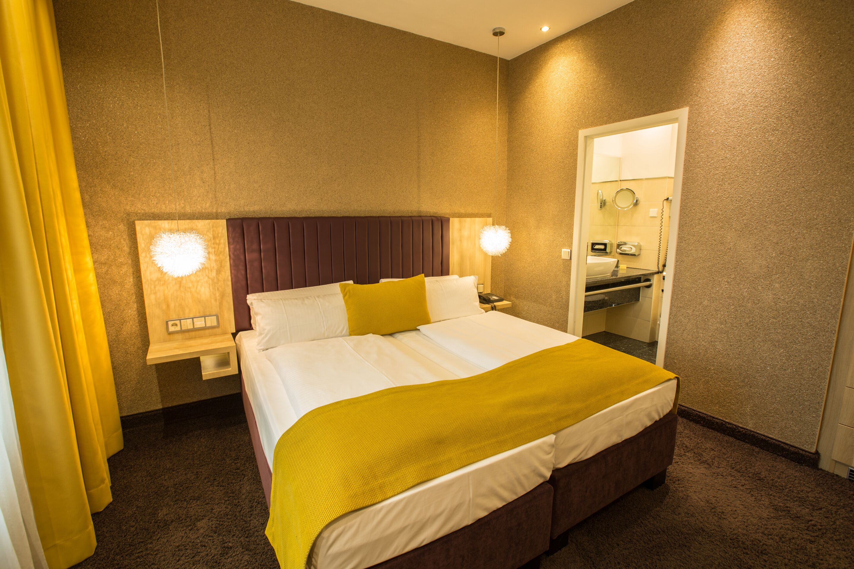 A hotel room with a large bed, a bedside table, a mirror, and a bathroom door.