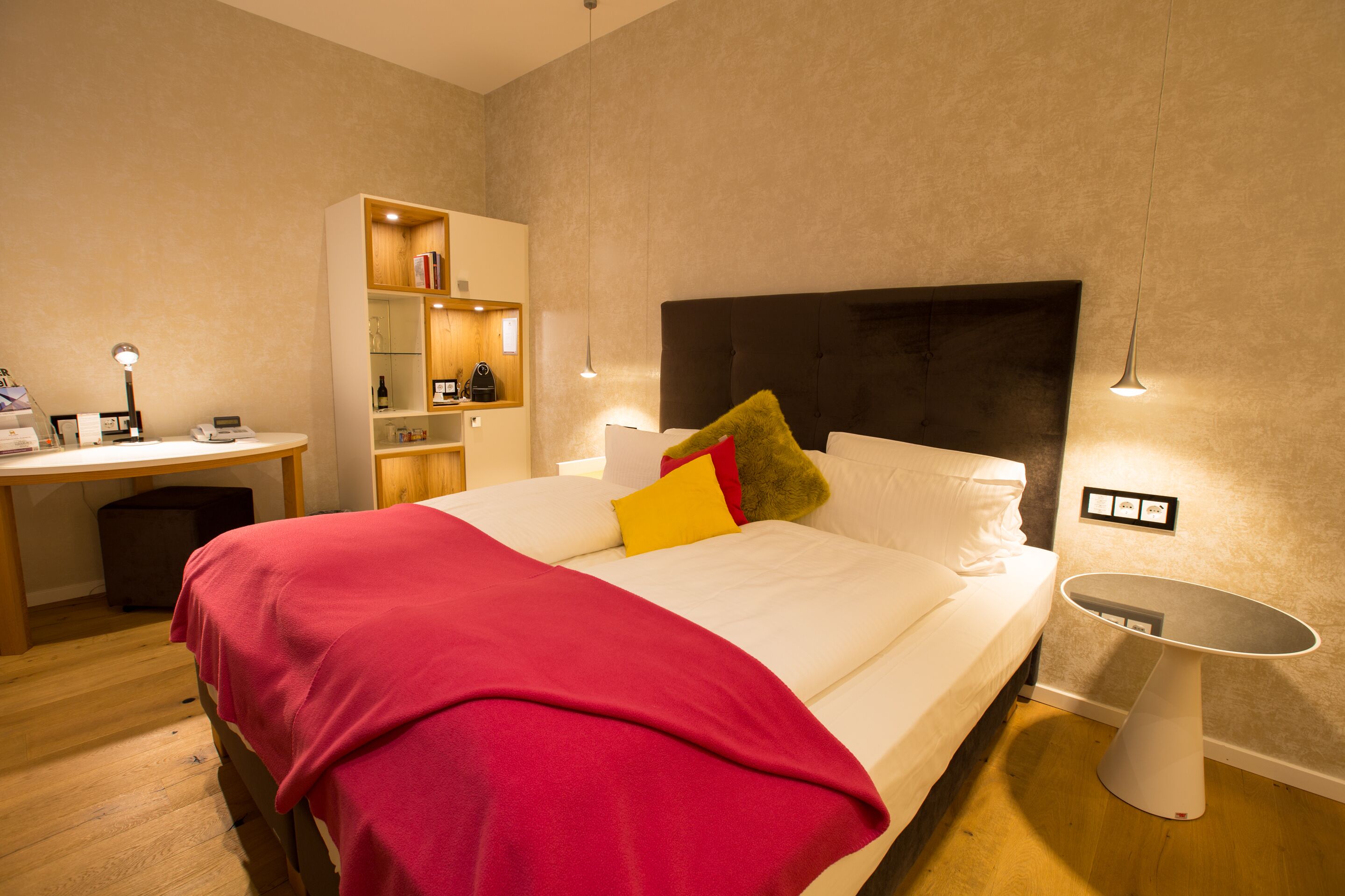 Una camera d'albergo con un letto, un comodino, una scrivania e degli scaffali.