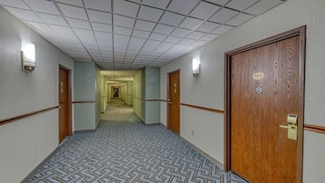 Um corredor de hotel com carpete estampado, portas de madeira e teto em azulejos.