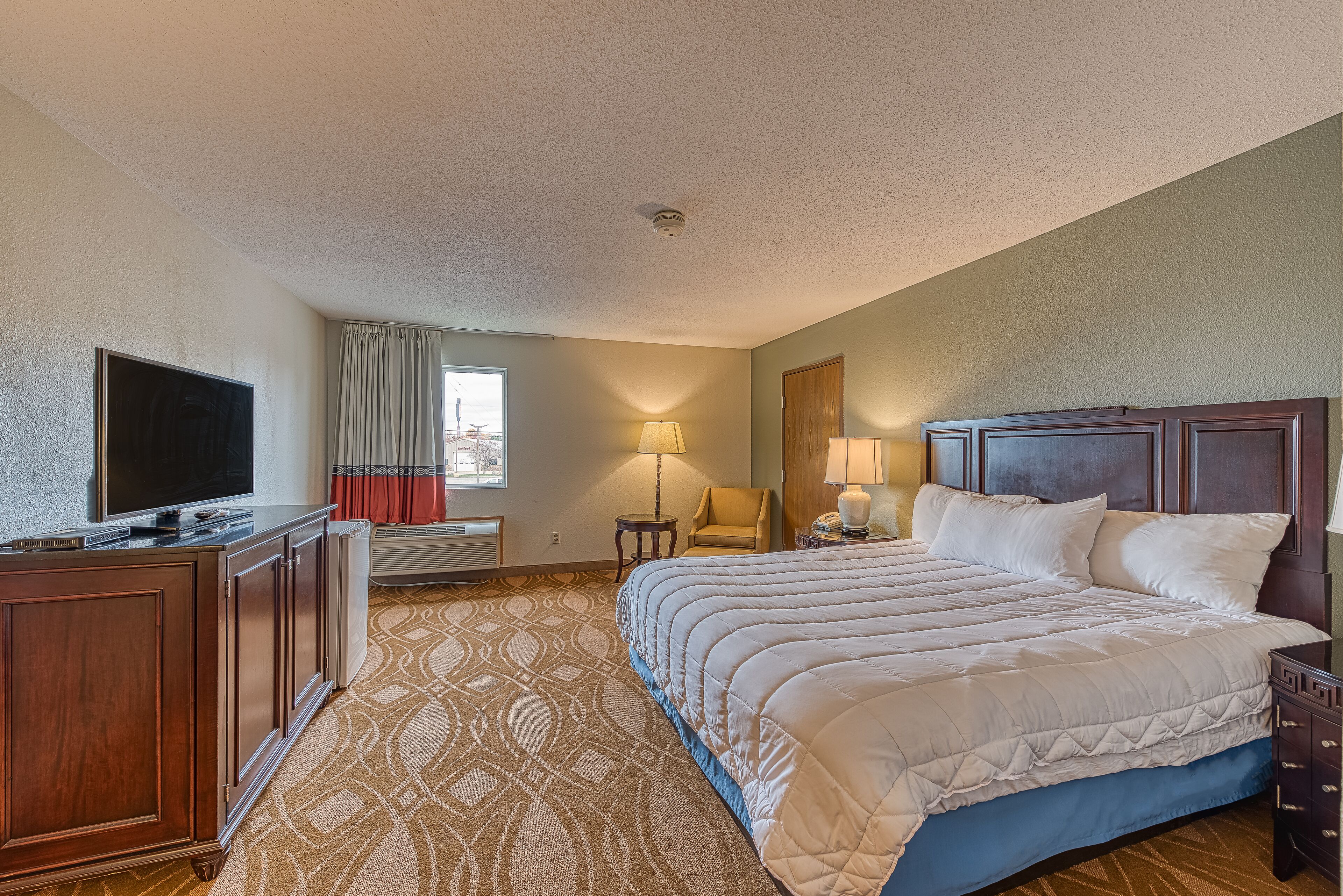 A hotel room with a large bed, a TV, a desk, and a lamp.