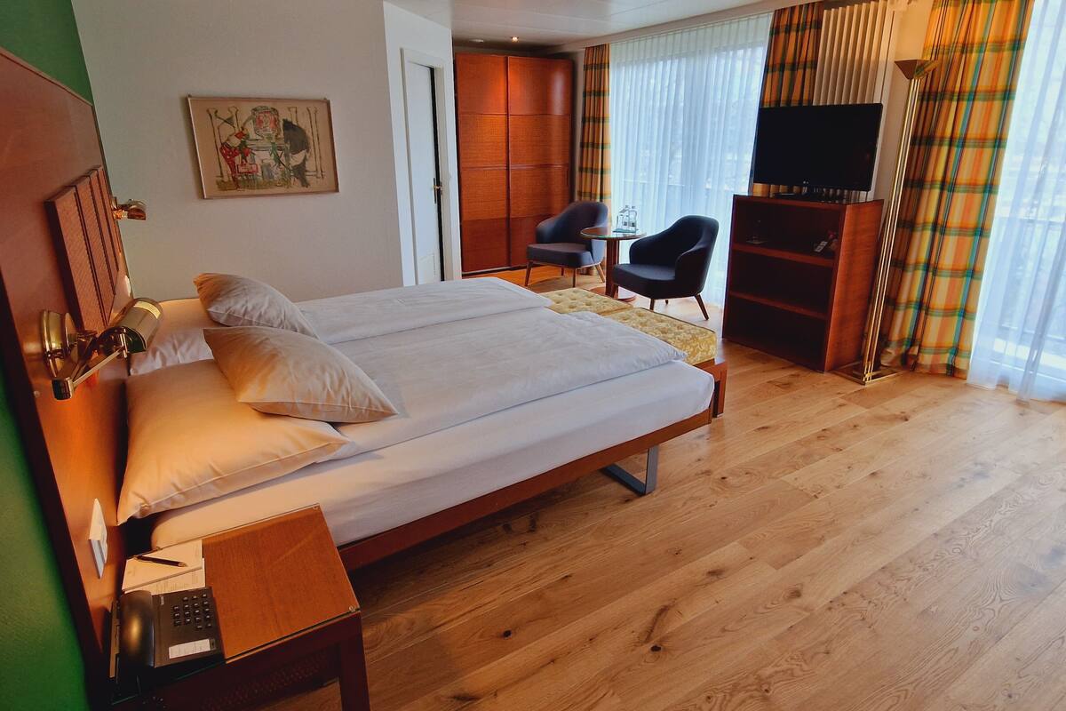 A hotel room with a large bed, a desk with a telephone, a chair, a television, and a bookshelf.