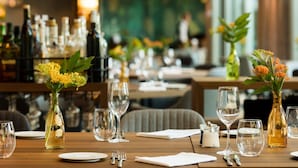 Un ambiente de restaurante con mesas dispuestas para comer, destacando cristalería y jarrones con flores.