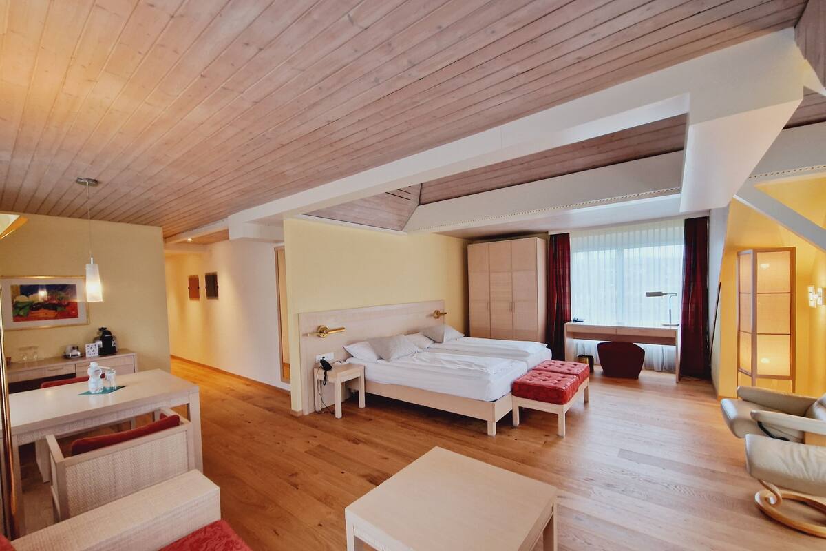 A modern hotel room with a wooden ceiling, a large bed, a desk, and a chair.