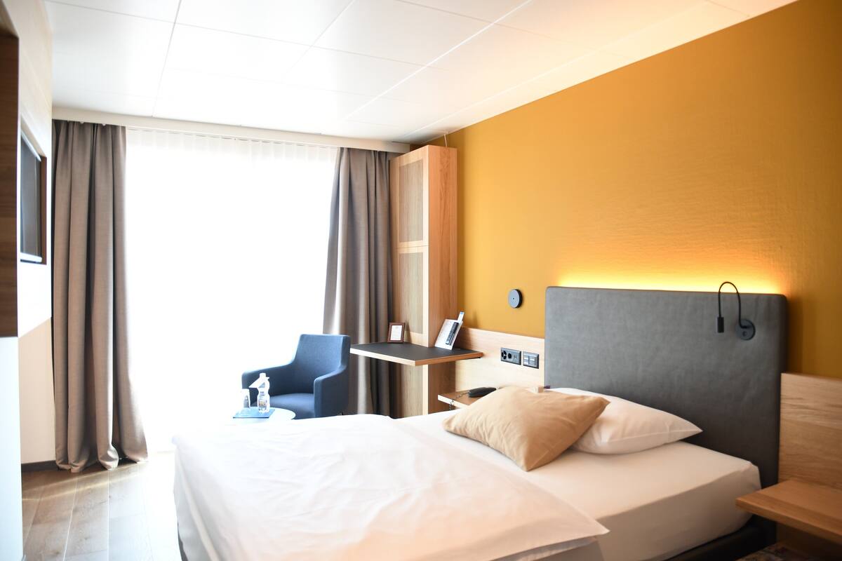 A hotel room with a bed, a desk, a chair, and a wardrobe.