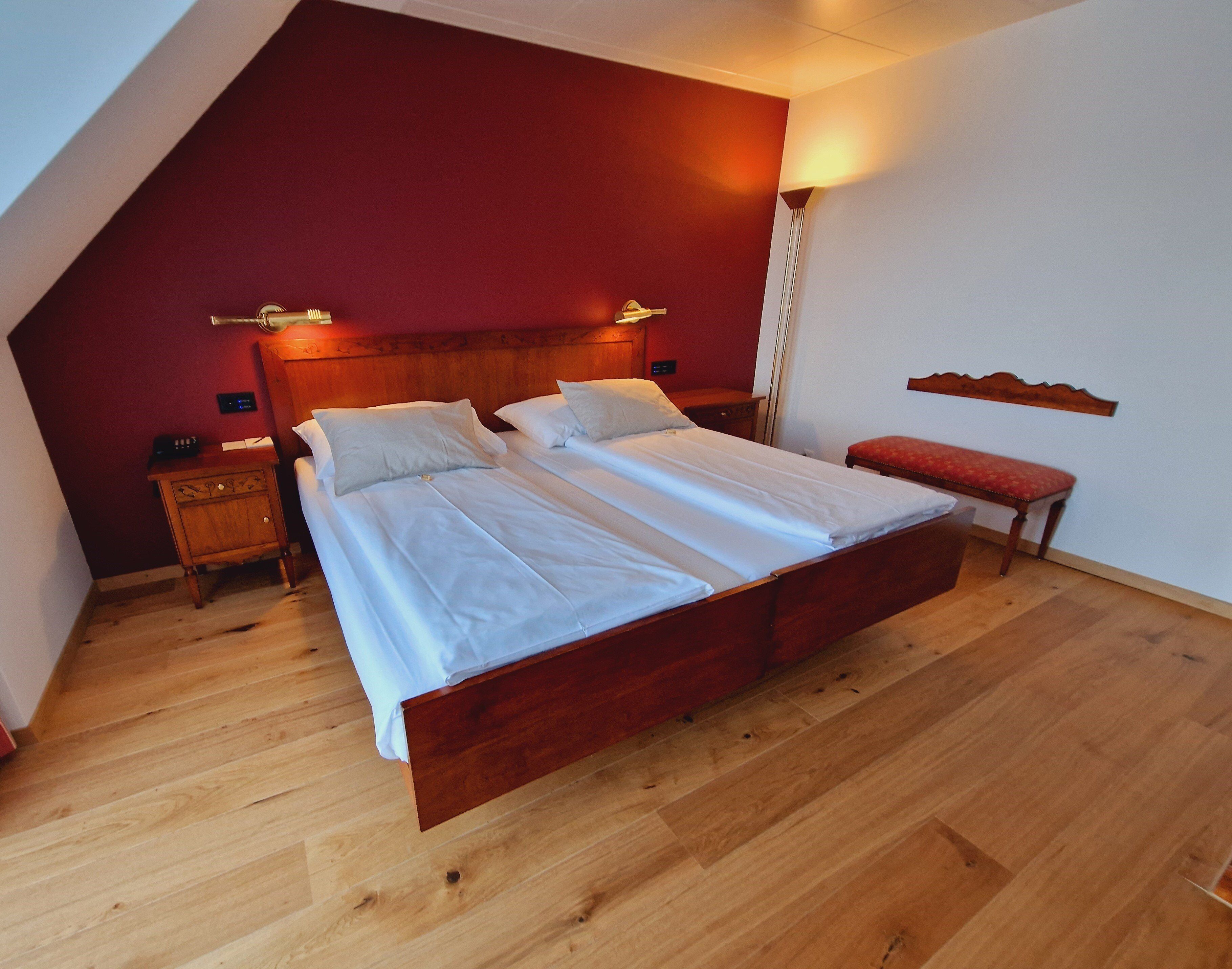 A bedroom with a wooden bed, two bedside tables, a bench, and a wall-mounted shelf.