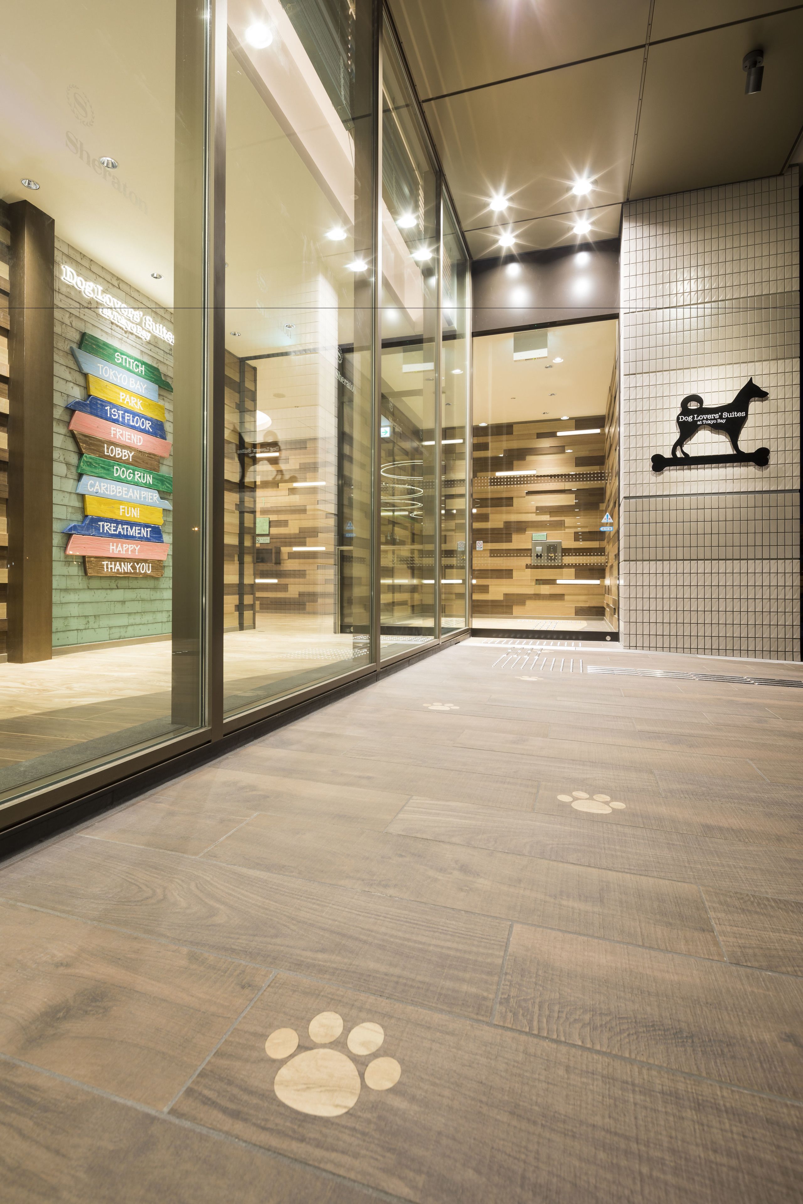 A modern lobby with glass doors, a wooden floor with paw print designs, and a wall with a dog logo.
