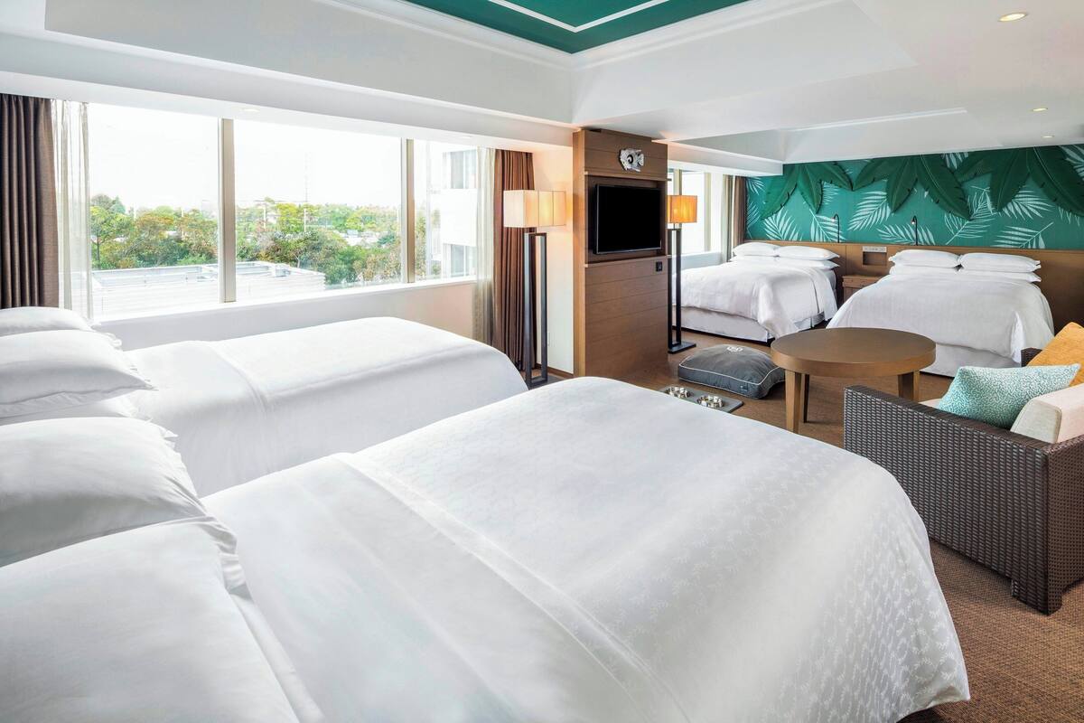 A hotel room with two beds, a TV, a small table, and a view of the outdoors.