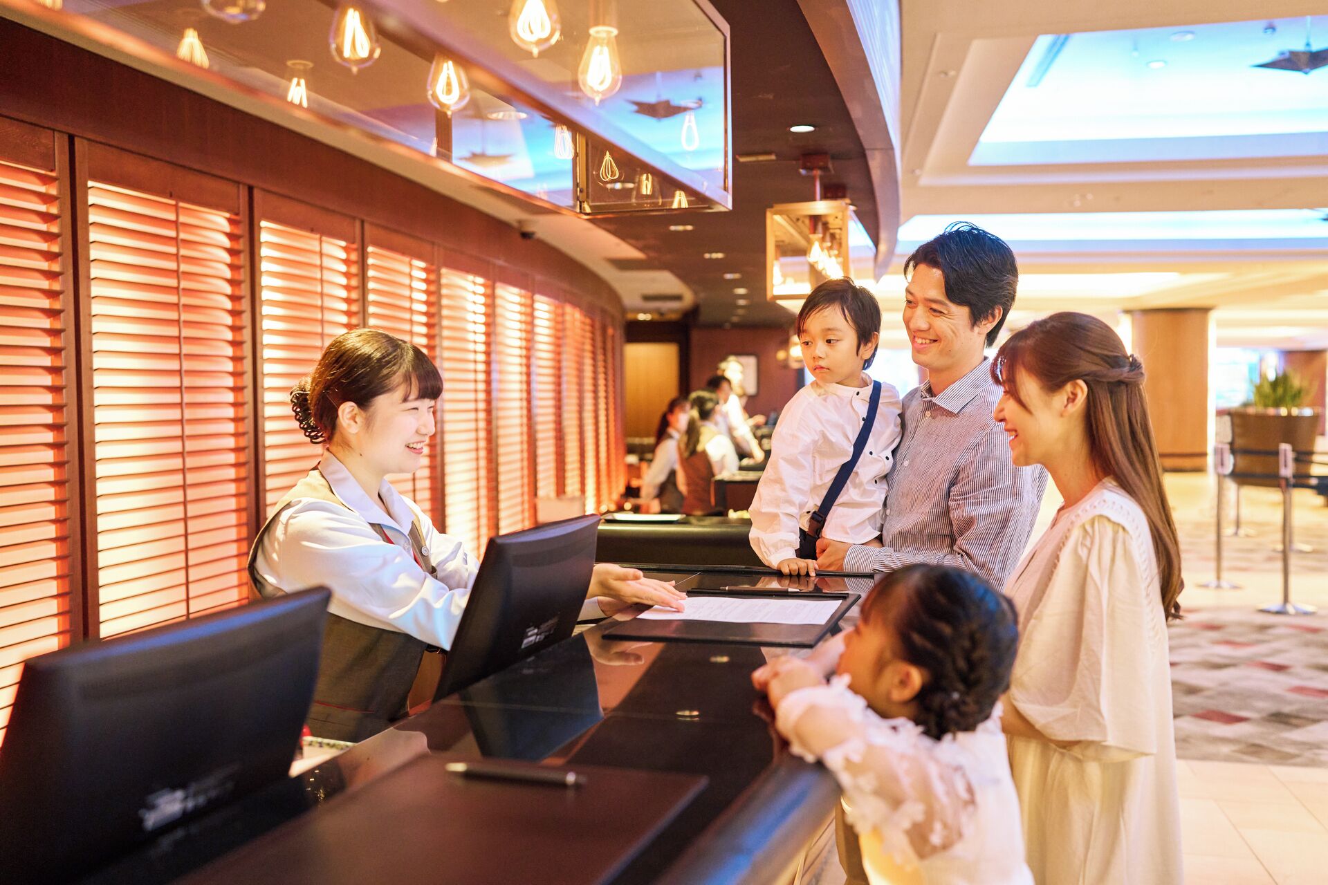 Un mostrador de recepción de hotel con una recepcionista, una familia y un niño.