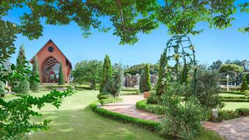 A garden with a red building, a white gazebo, and neatly trimmed hedges.