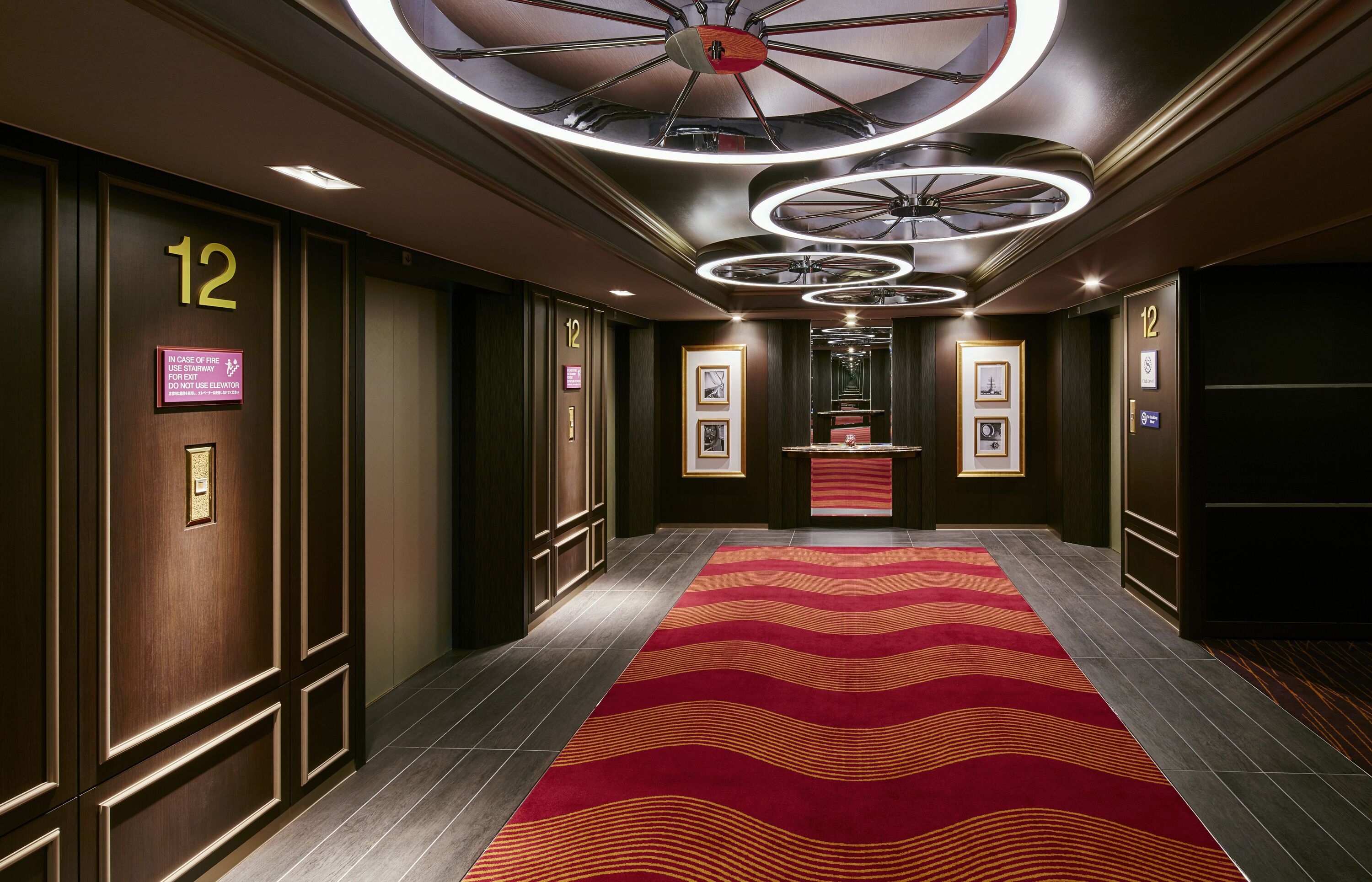 Un corridoio con tappeto rosso, pannelli di legno e un soffitto con lampade circolari.