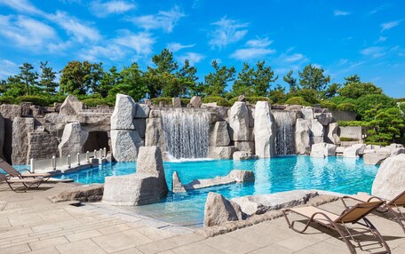 A swimming pool with a waterfall feature, surrounded by stone structures and trees.
