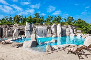 Une piscine agrémentée d’une cascade, entourée de constructions en pierre et d’arbres.
