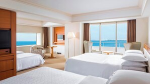 Habitación de hotel con dos camas, televisión, escritorio y vistas al mar.