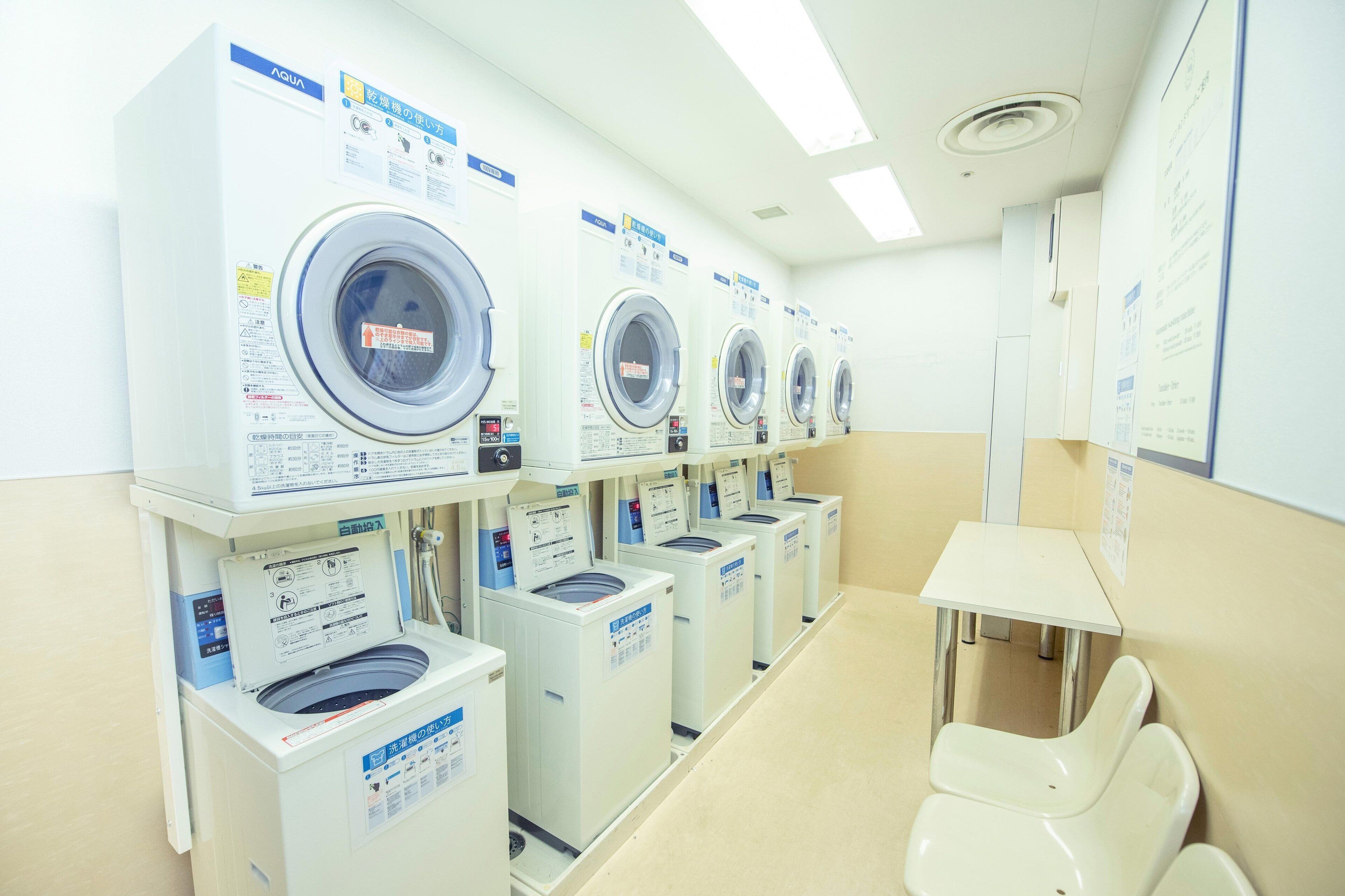 A row of front-loading washing machines in a laundry room with a table and chairs.