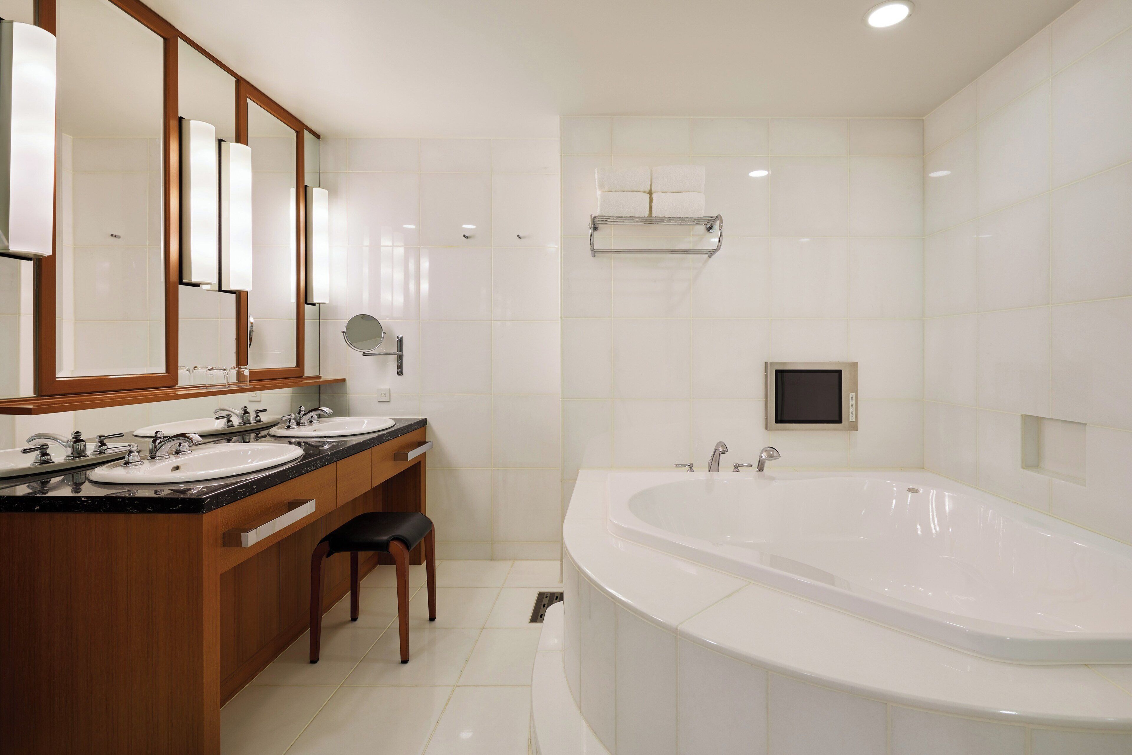 A modern bathroom with two sinks, a large bathtub, and a mirror with a built-in light.