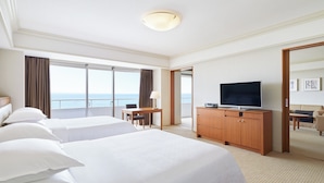 Habitación de hotel con dos camas, televisión, escritorio y vista al mar.