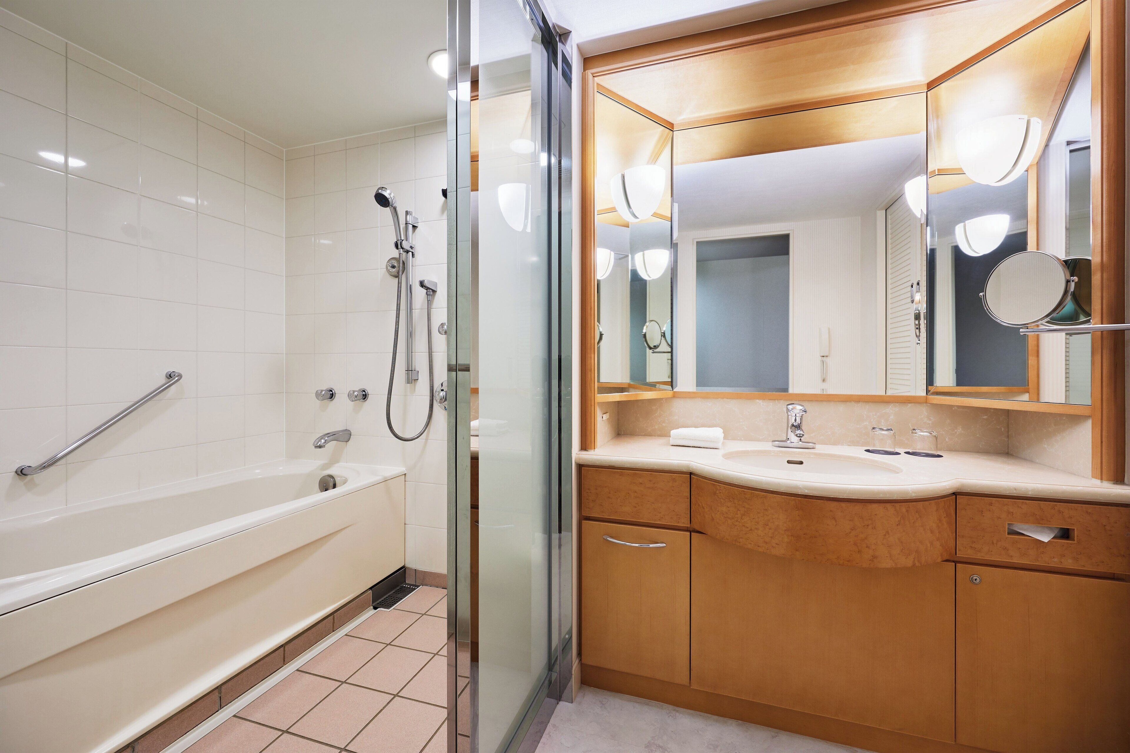 A modern bathroom with a bathtub, a glass shower enclosure, wooden cabinets, and a large mirror.