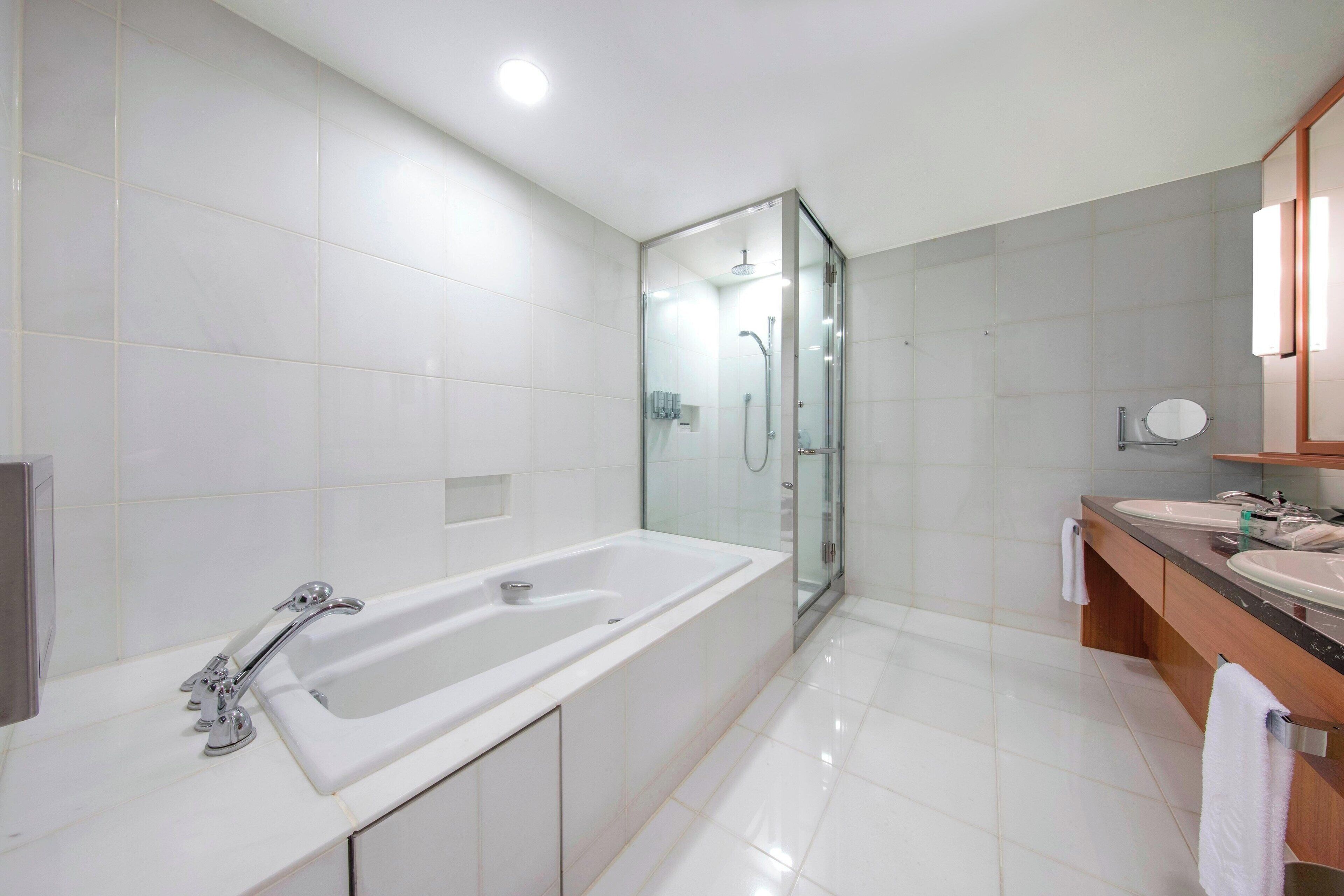 A modern bathroom with a glass-enclosed shower, a large white bathtub, and a wooden vanity with two sinks.