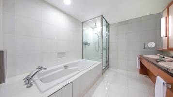 A modern bathroom with a glass-enclosed shower, a large white bathtub, and a wooden vanity with two sinks.