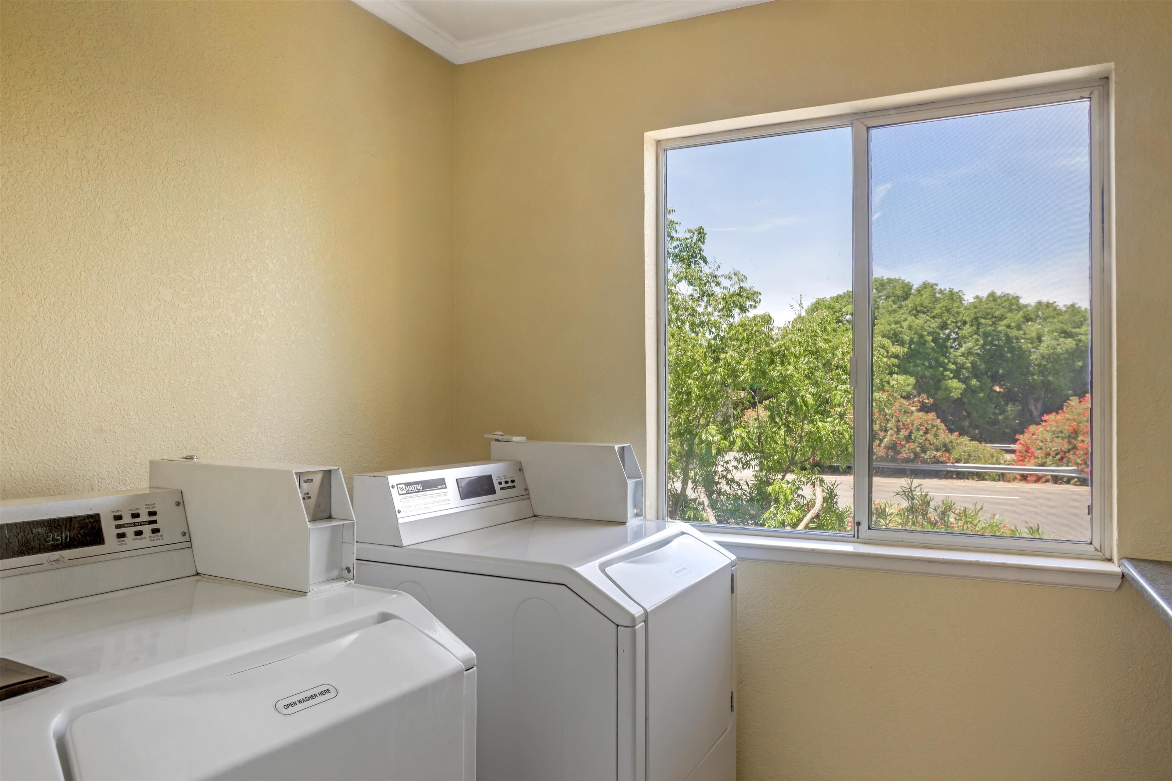 A laundry room with two washing machines and a large window offering a view of trees and a parking lot.