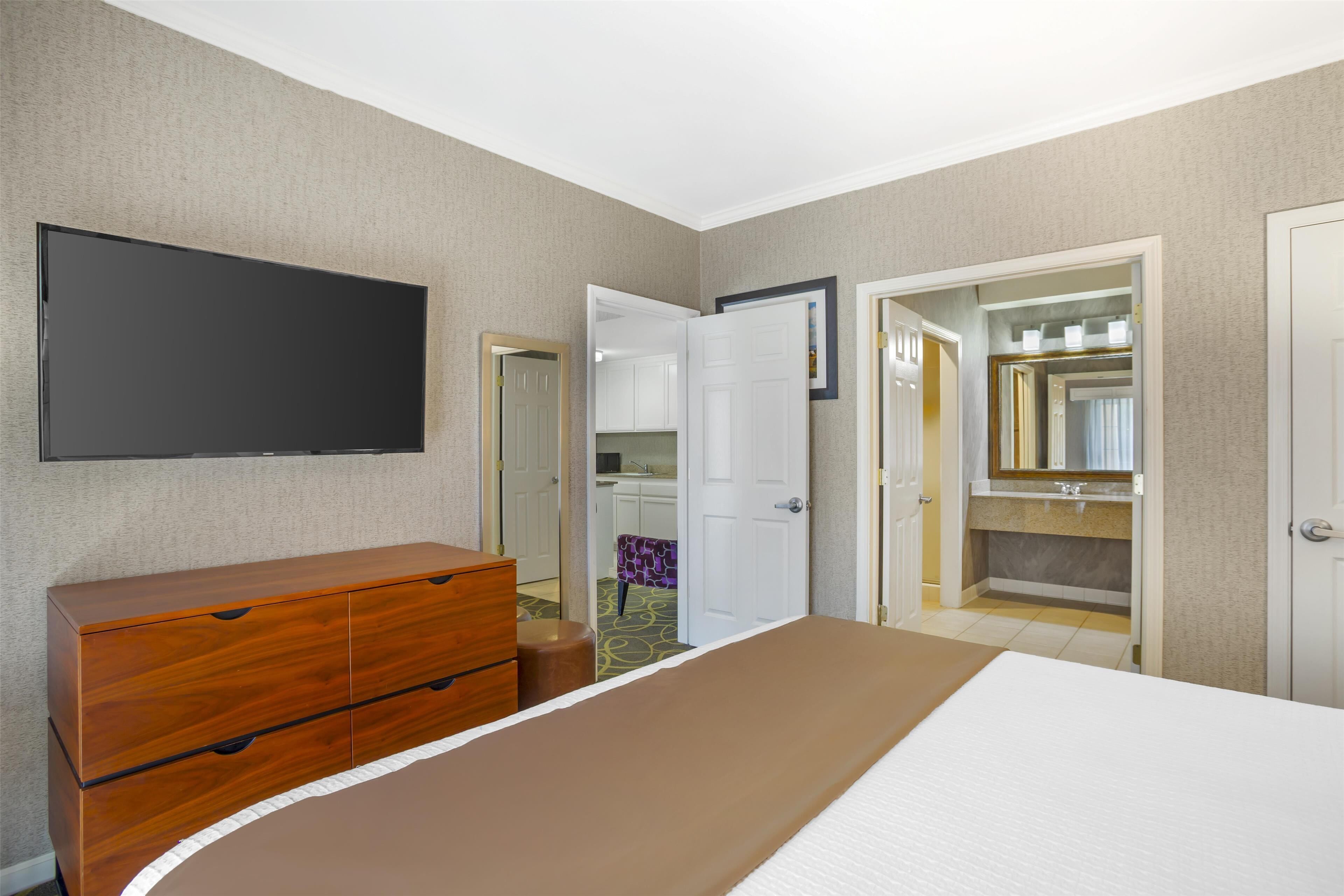 A hotel room with a bed, a wooden dresser, a television, and a bathroom with a mirror and sink.