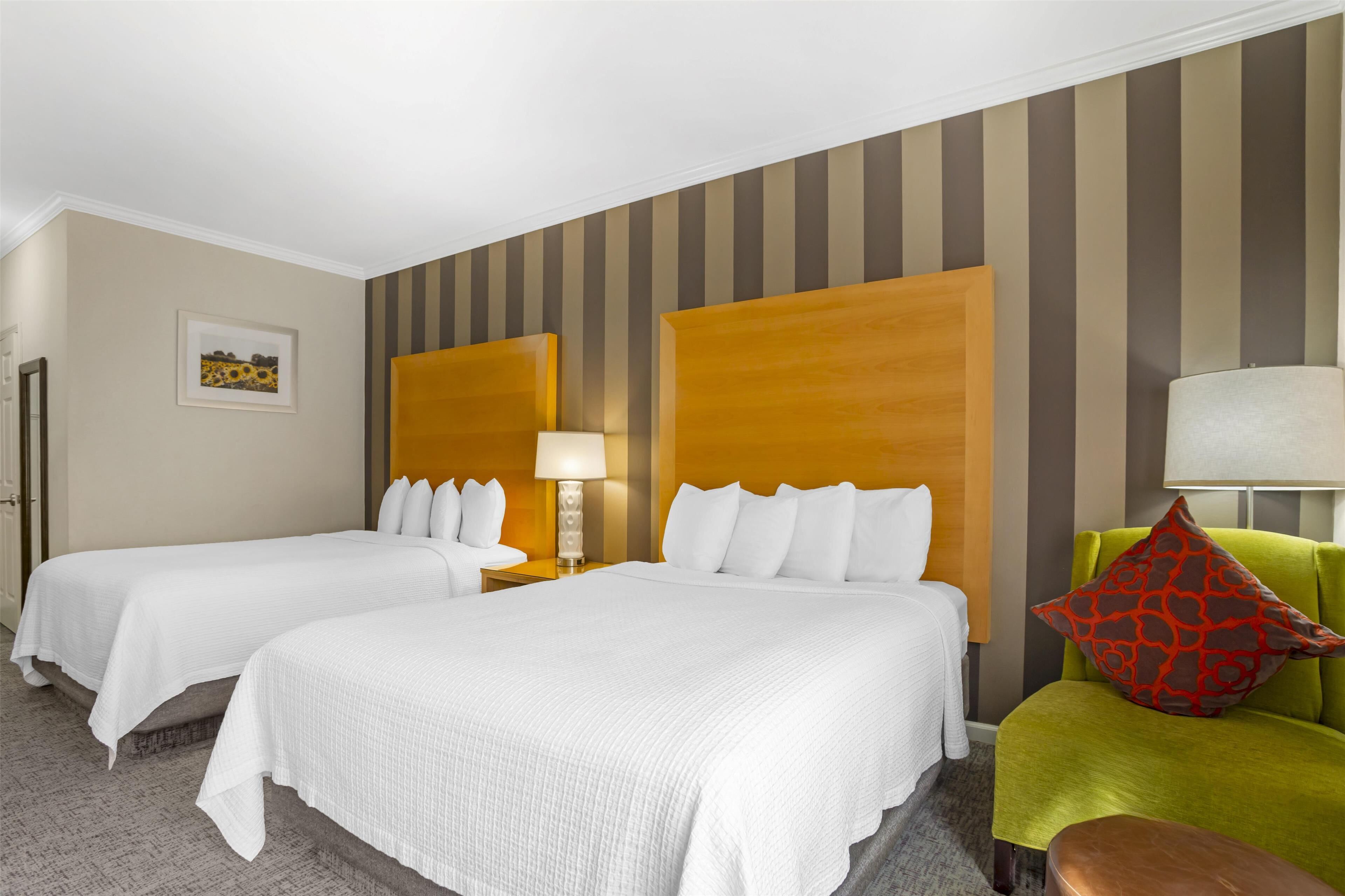 A hotel room with two beds, a green armchair, and a wooden headboard.
