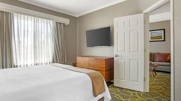 A hotel room with a bed, a dresser, a television, and a door leading to another room.