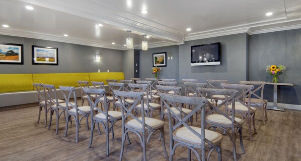 Un salón de conferencias con filas de sillas de madera, un sofá amarillo, un televisor de pantalla plana y obras de arte enmarcadas en las paredes.