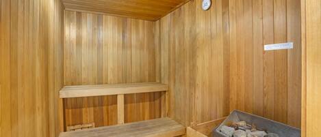 Una sauna de madera con bancos y un recipiente lleno de piedras, probablemente para calentar.