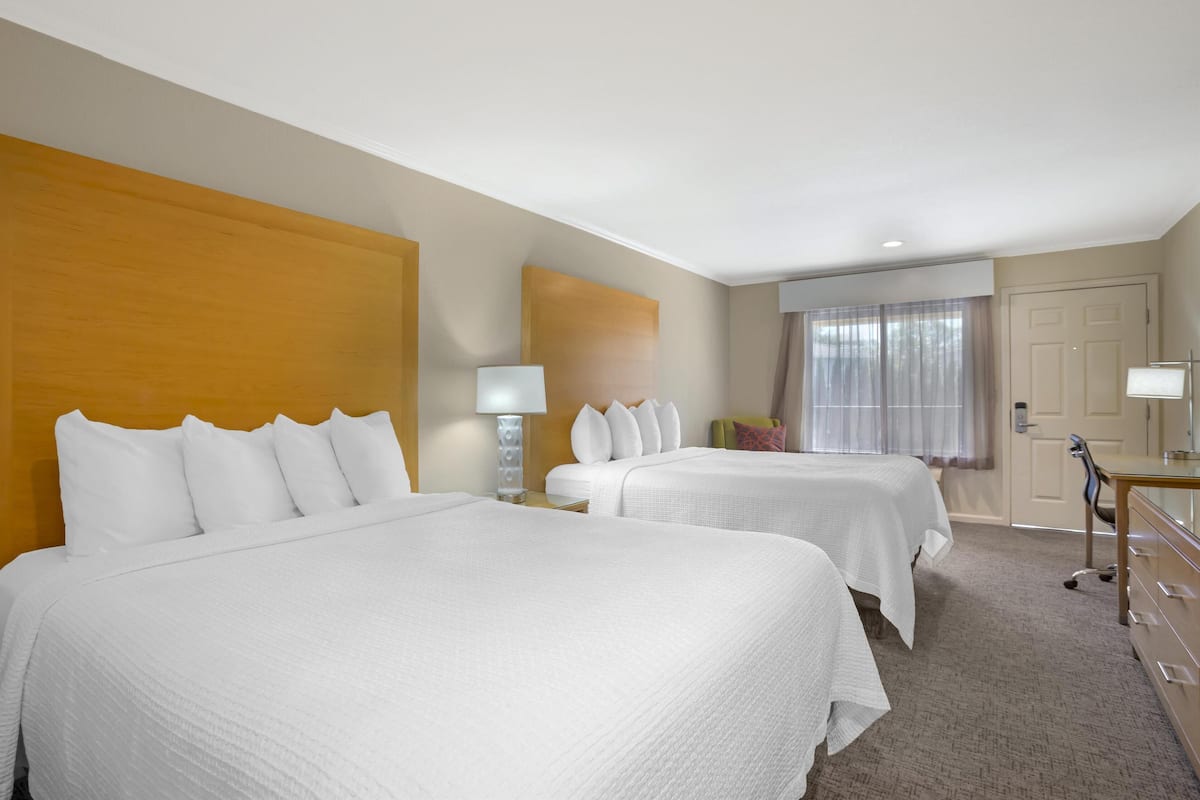 Une chambre d’hôtel avec deux lits, un bureau avec une chaise, un miroir et une fenêtre avec des rideaux.