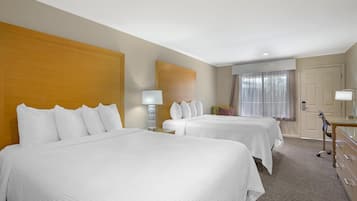 A hotel room with two beds, a desk with a chair, a mirror, and a window with curtains.